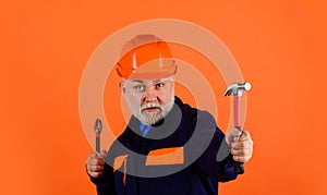 Construction worker or builder in safety hard hat with adjustable wrench and hammer. Bearded man in uniform with