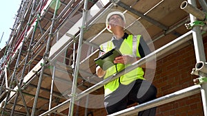 Construction worker on building site standing on scaffolding writing on a clipboard