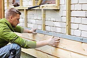 Construction worker checking level of house wood facade