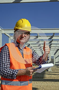 Construction Worker With Clipboard Giving Thumbs Up At Construction Site