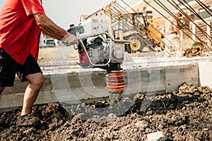 Construction worker compacting soil with vibration compaction machine