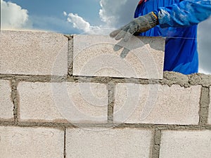Construction worker in construction site is building wall by cement block isolated on blue sky background closeup.