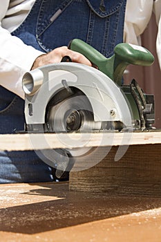 The carpenter cuts the board with a manual electric saw.