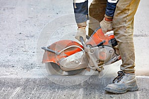 A construction worker cuts old asphalt with a portable petrol saw and a diamond cutting disc