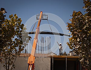 A construction worker directing a large load of pipe on a crane at a construction site