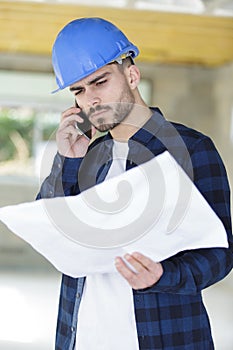 Construction worker discussing on phone something related to plans