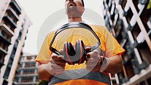 Construction worker with ear muff working at construction site. Worker puts on ear defenders to protect against sound. Taking care