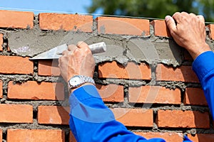 Bricklayer using a trowel to apply mortar to a new brick wall