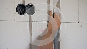 Construction worker fitting plastic pipe for electric cables into chase groove in white concrete bricks wall, detail on hands only