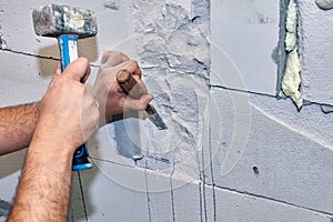 Construction worker gouges niche in concrete wall using hammer and chisel.