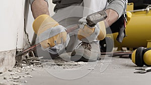 Construction worker hands with gloves working with hammer and chisel to remove old plaster from wall for house renovation, close