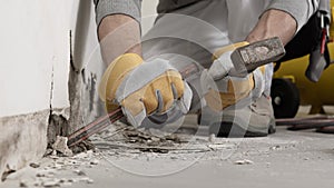 Construction worker hands with gloves working with hammer and chisel to remove old plaster from wall for house renovation, close