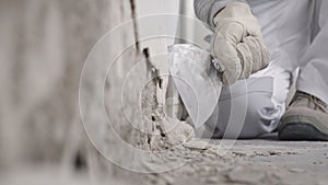 Construction worker hands with gloves working with spatula scrape off the plaster from the wall for house renovation, close up photo