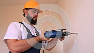 Construction worker and handyman with blue electric drill drills a nail hole into wall of construction site.