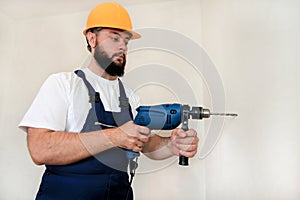 Construction worker, handyman and builder with blue electric drill drills a nail hole into wall of construction site.