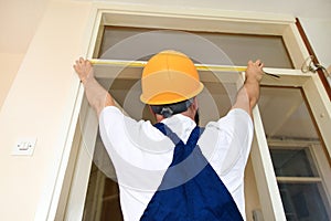 Construction worker and handyman is working on renovation of apartment. Builder is measuring of room door using measure tape.