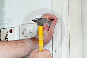 Construction worker and handyman with yellow hammer strikes and nails a nail into wooden wall of kitchen door at construction site