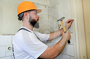 Construction worker and handyman with yellow hammer strikes and nails a nail into wooden wall of kitchen door at construction site