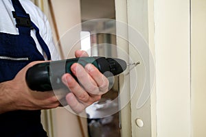 Construction worker and handyman works on renovation of apartment. Builder with electric drill drills nail hole into wall door.