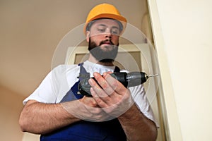 Construction worker and handyman works on renovation of apartment. Builder with electric drill drills nail hole into wall door.