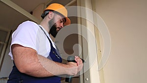 Construction worker and handyman works on renovation of apartment. Builder with electric drill drills nail hole into wall door.