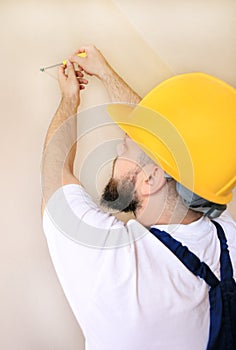 Construction worker and handyman works on renovation of apartment. Builder using yellow screwdriver screws steel screw out of wall