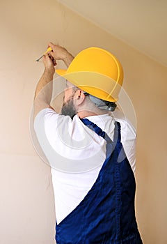 Construction worker and handyman works on renovation of apartment. Builder using yellow screwdriver screws steel screw out of wall