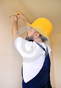 Construction worker and handyman works on renovation of apartment. Builder using yellow screwdriver screws steel screw out of wall