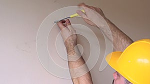 Construction worker and handyman works on renovation of apartment. Builder using yellow screwdriver screws steel screw out of wall