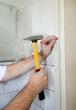 Construction worker and handyman with yellow hammer strikes and nails a nail into wooden wall of kitchen door at construction site