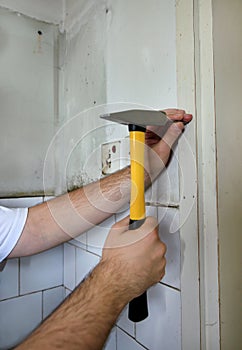 Construction worker and handyman with yellow hammer strikes and nails a nail into wooden wall of kitchen door at construction site