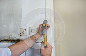 Construction worker and handyman with yellow hammer strikes and nails a nail into wooden wall of kitchen door at construction site