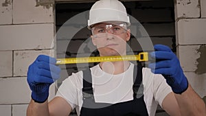 A construction worker in a helmet and glasses holding a measuring tape measure.