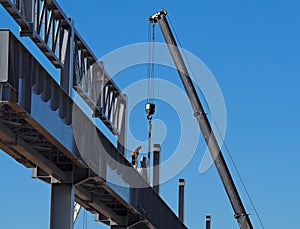 Construction worker, with the help of a mobile telescopic crane, builds the metal structure of an elevated infrastructure