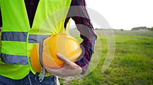 Construction worker holding his yellow helmet wearing fluorescent waistcoat on the empty field (OSH).