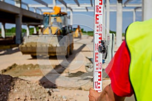 Worker is holding leveling rod to measuring level on construction site