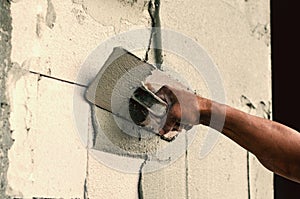 Construction worker holding plastering trowel smoothing wall defects