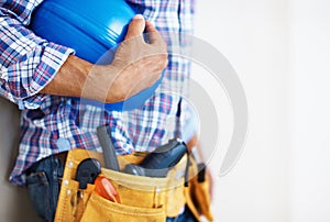 Construction worker holding protective helmet. Mid section of construction worker with tool belt holding blue protective