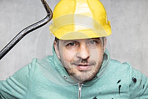 The construction worker holds a work tool in his hands, a crowbar