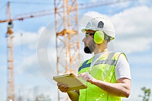 Construction worker or inspector engineer with tablet on building site in protecting sefety equipment