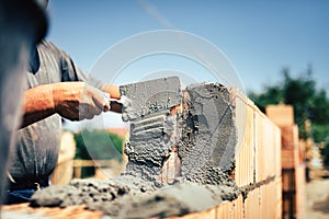 Construction worker installing brick masonry on exterior wall with trowel putty knife