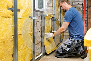 Construction worker insulating brick wall with glass wool