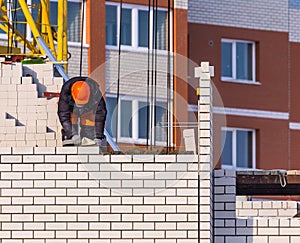 Construction Worker Laying Bricks and wearing an orange hard hat.