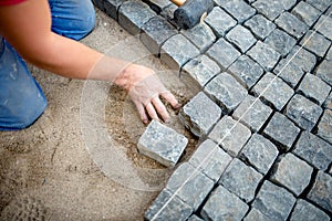 Construction worker laying cobblestones and stone blocks on pavement photo