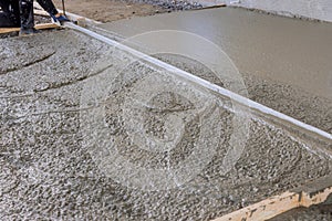 A construction worker in leveling an poured concrete with using long trowels is wet cement sidewalk