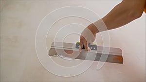 Worker aligns the wall with a spatula and putty. Construction worker with a long spatula plastering a wall