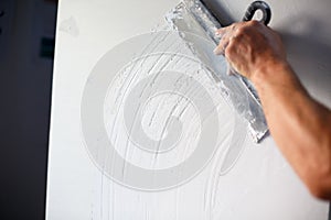 Construction worker with long trowel plastering a wall.