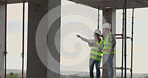 Construction worker man and architect woman in a helmet, discuss the plan of construction of house, tell each other