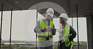 Construction worker man and architect woman in a helmet, discuss the plan of construction of house, tell each other