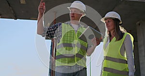 Construction worker man and architect woman in a helmet, discuss the plan of construction of house, tell each other